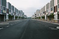 A quiet, empty urban street flanked by modern condominiums under a cloudy sky, with ample parking space.